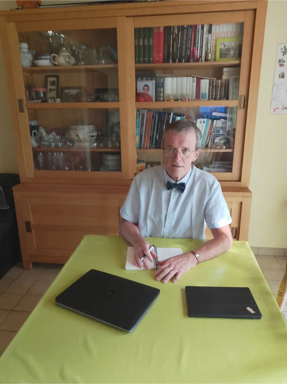 Roland Cotty, écrivain, assis à son bureau en train d’écrire, devant une bibliothèque.